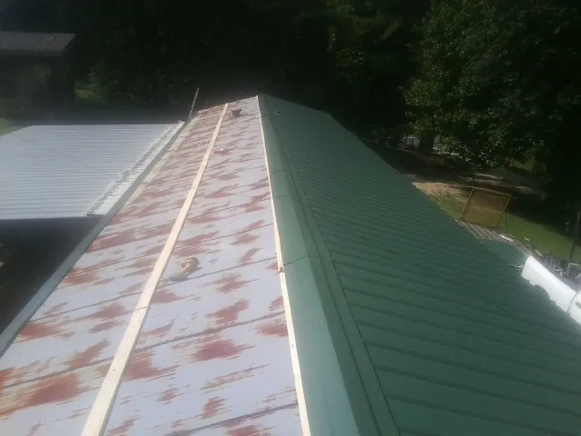 Old rusted panels beside newly installed green metal roofing — Wind Damage Roof Repair by Roofing Brothers in Hot Springs