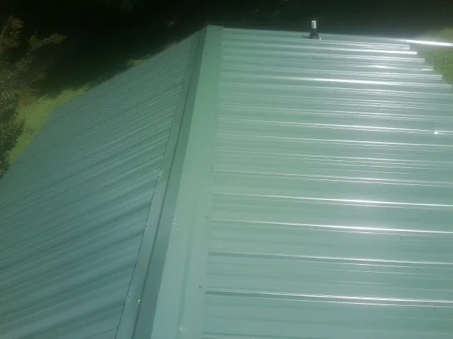 New green metal panels meeting at the ridge of a roof — Flat Roof Repair work by our crew in Hot Springs