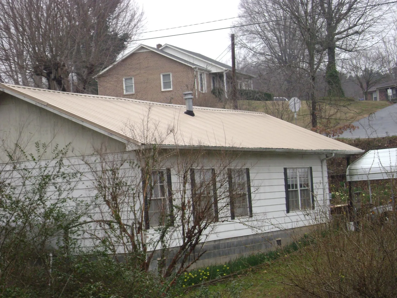 Tan metal roof on a white sided house set into a hillside — Commercial Roofing by Roofing Brothers in Hot Springs