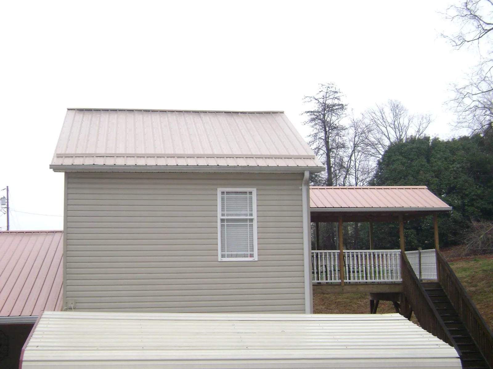 Tan metal roofs on a two story addition and attached porch, from a Roof Replacement job in Hot Springs